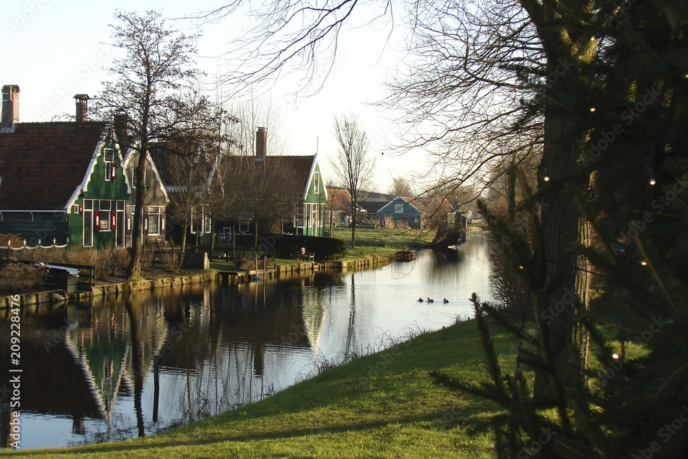 typical street in a traditional Dutch village with small wooden houses, lawns and canals; Zaanse Schans (Netherlands); green winter typical street in a traditional Dutch village with small wooden houses, lawns and canals; Zaanse Schans (Netherlands); green winter