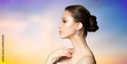 beauty  jewelry  people and luxury concept - close up of beautiful asian woman face with earring over pastel background