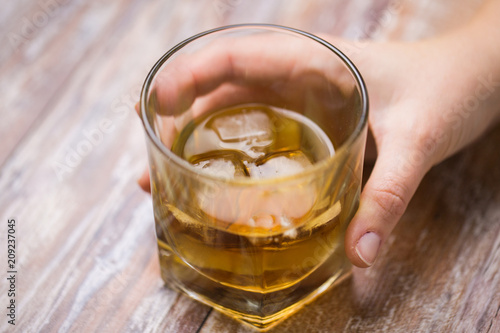 alcoholism, alcohol addiction and people concept - close up of male hand with glass of whiskey on table