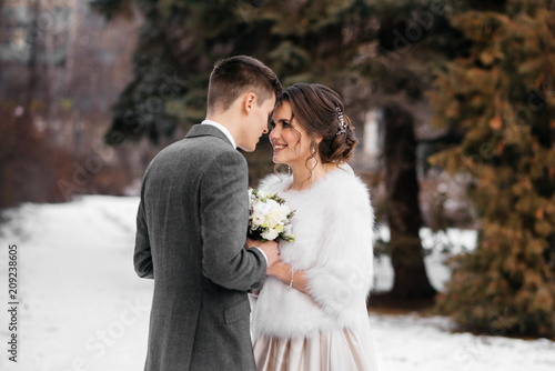 The bride and groom stand in the winter park, huddled together
