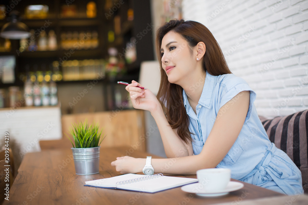 Young business woman sitting at table in cafe and writing in notebook and cup of coffee. Freelancer working in coffee shop. - obrazy, fototapety, plakaty 