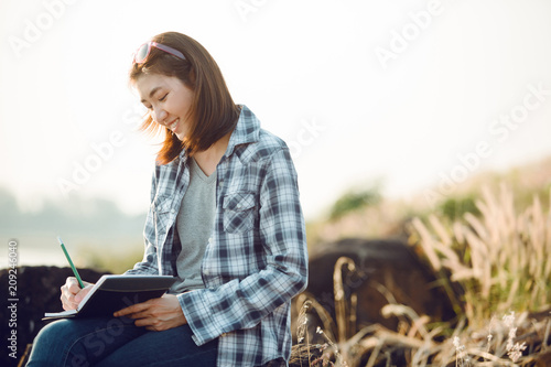 Beautiful young Asia woman writing on a journal about her hiking trip,flare light