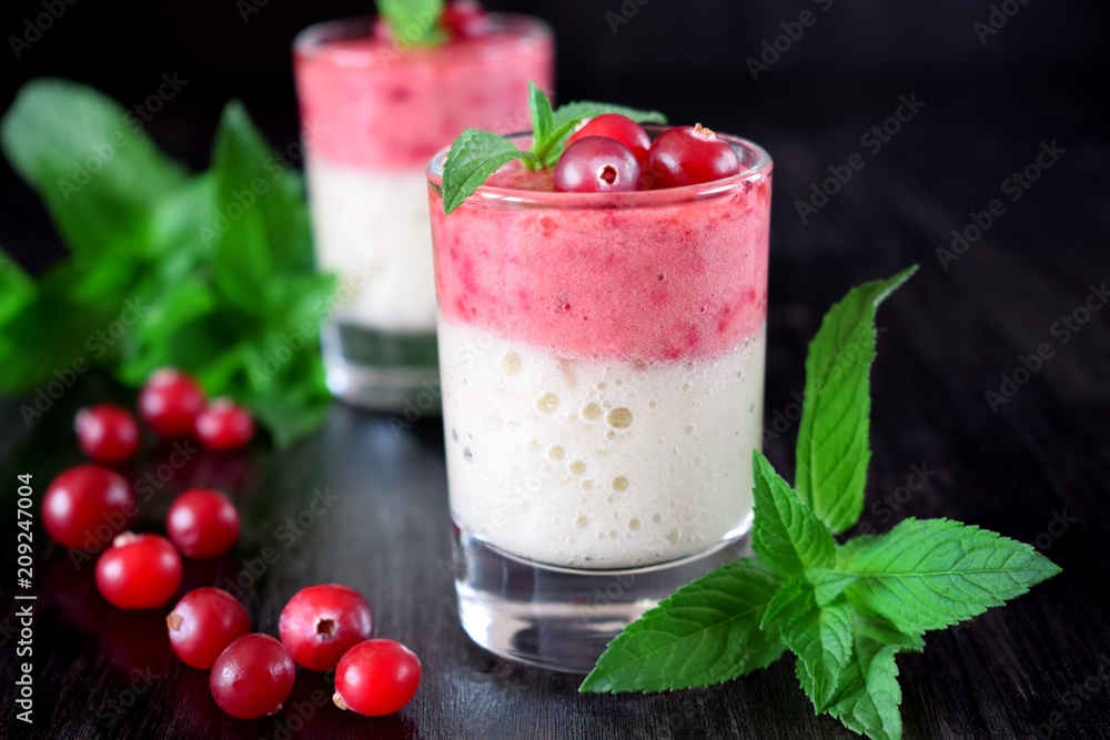 Two layered smoothie in glasses surrounded by cranberries and mint against the dark background Two layered smoothie in glasses surrounded by cranberries and mint against the dark background