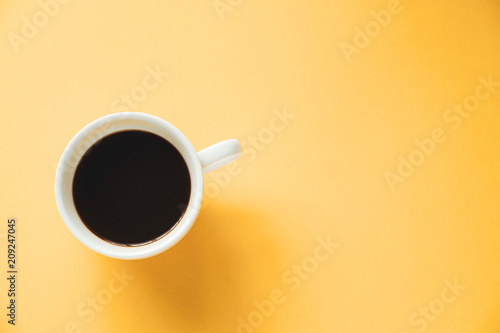 Hot black coffee in white cup on yellow background