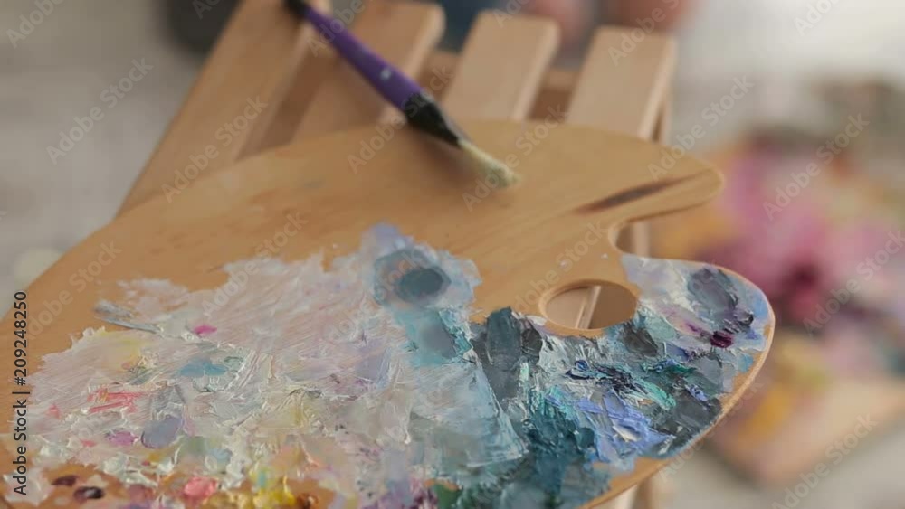 Artistic equipment: easel, paint brushes, tubes of paint, palette and paintings on work table in a artist studio. Palette with paints and brushes for drawing. Artistic equipment: easel, paint brushes, tubes of paint, palette and paintings on work table in a artist studio. Palette with paints and brushes for drawing.