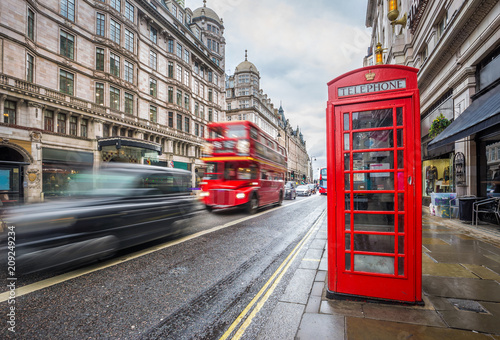 London, England - Iconic blurred black londoner taxi and vintage red double-decker bus on the move with traditional red telephone box in the center of London at daytime photo