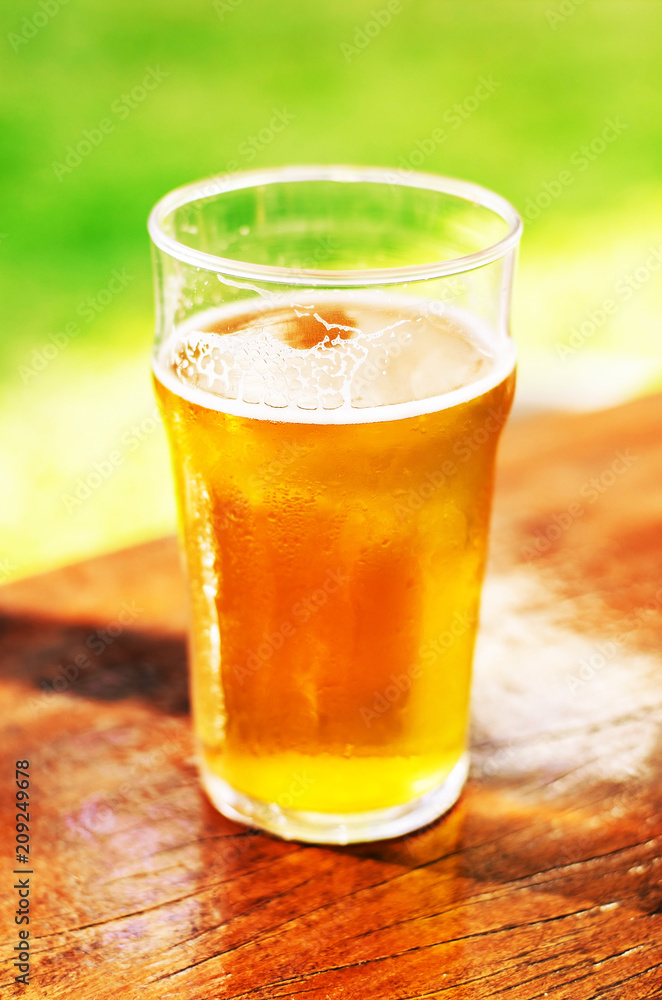 Glass of 500 ml of draft beer with no foam over a wooden table on a sunny day. Glass of 500 ml of draft beer with no foam over a wooden table on a sunny day.