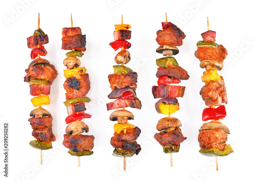 Roasted pork skewers with bacon, diced red, yellow, green bell pepper, champignons and onion stuffed on wooden sticks. Colorful mix of tasty pork barbecue on white background