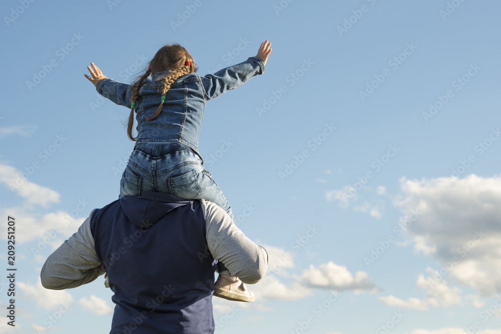 Father and his daughter playing outdoors. the child sits at the daddy on the neck, having lifted hands. against the sky. Happy loving family. Father's Day Father and his daughter playing outdoors. the child sits at the daddy on the neck, having lifted hands. against the sky. Happy loving family. Father's Day