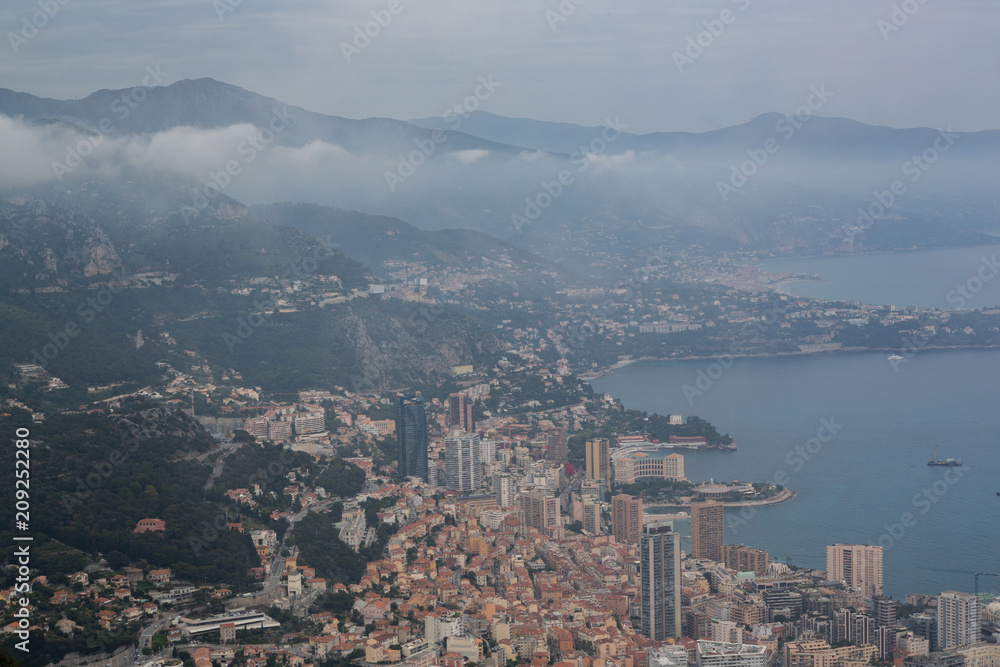 Scenic panorama of Monaco from the observation deck. Roofs of houses and buildings and hills on background. Sailing boats and yacht harbour, port. Aerial top view, foggy morning. France