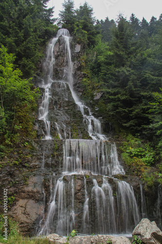 Waterfall in mountain forest with silky foaming water and wet stones