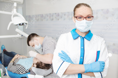 Portrait of female dentist with tools  in her dentist office and looking at camera.   Medicine  stomatology  healthcare concept.  Doctor doing dental treatment on man s teeth in the dentists chair.