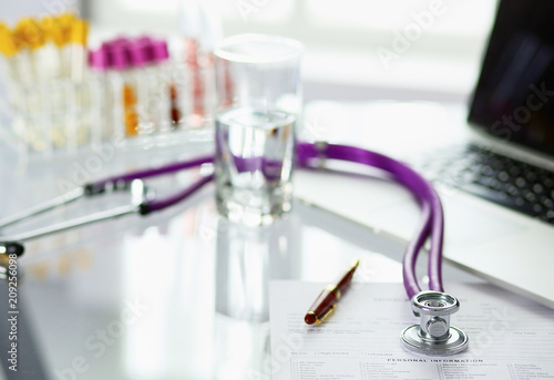 closeup of the desk of a doctors office with a stethoscope in the foreground and a bottle with pills in the background, selective focus