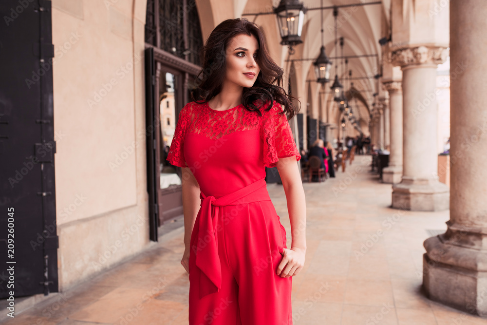 Photo of beautiful stylish brunette woman in the city ,wearing red jumpsuit. Fashion summer photo