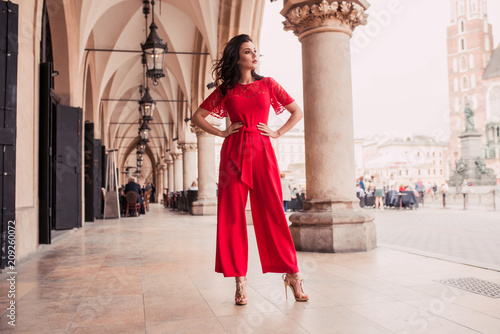 Photo of beautiful stylish brunette woman in the city ,wearing red jumpsuit. Fashion summer photo