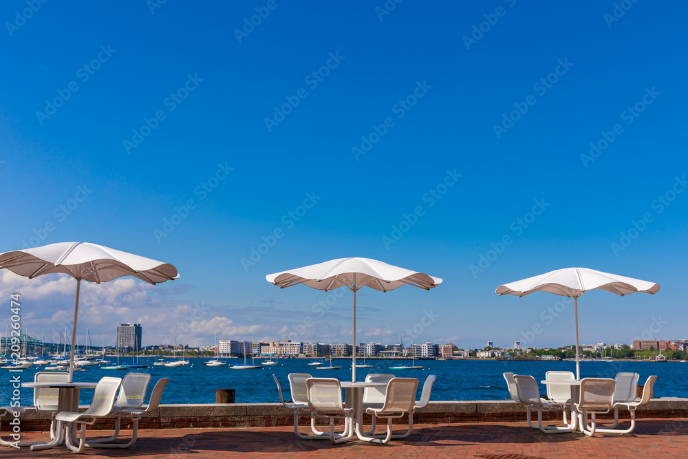 Tables with umbrellas on sunny day at Fan Pier Park Boston, Massachusetts.  Close to sea