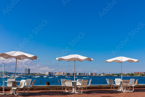 Tables with umbrellas on sunny day at Fan Pier Park Boston, Massachusetts. Close to sea