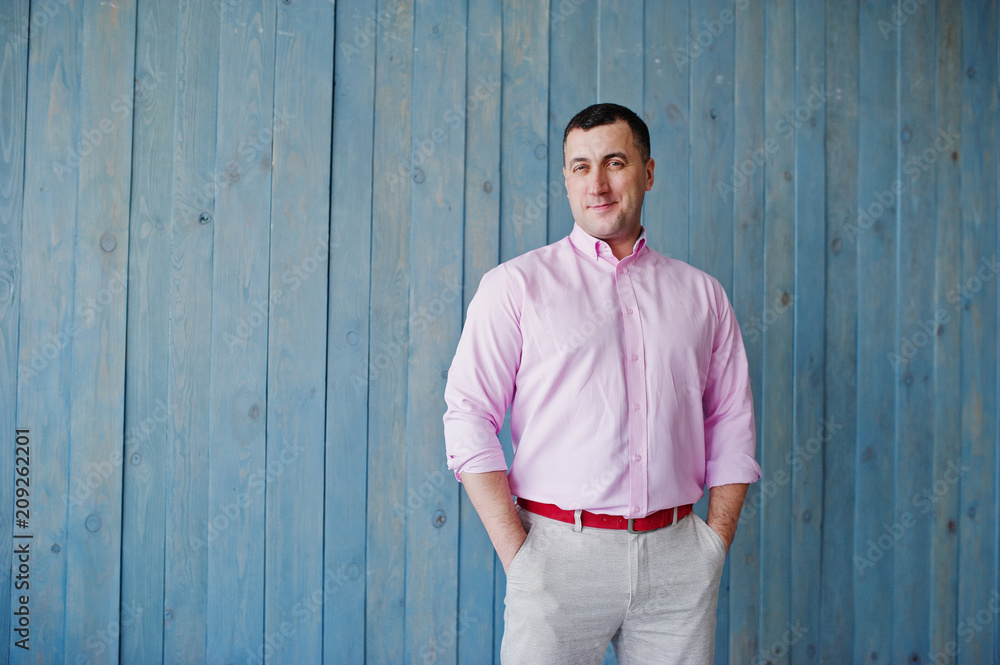 Studio portrait of man in pink shirt against wooden background. Studio portrait of man in pink shirt against wooden background.