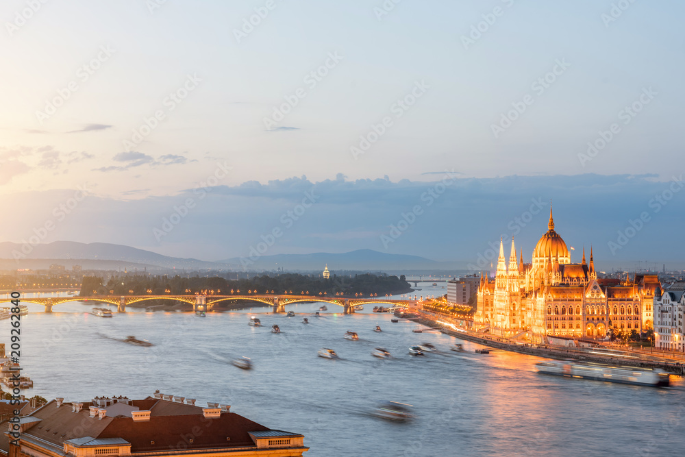 Aerial cityscape view with motion blurred ships and illuminated Parliament building during the twilight in Budapest, Hungary