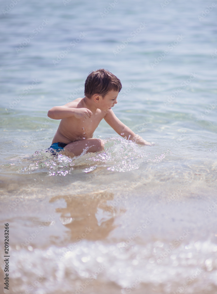 Adorable young kid sitting in the water on the beach Adorable young kid sitting in the water on the beach