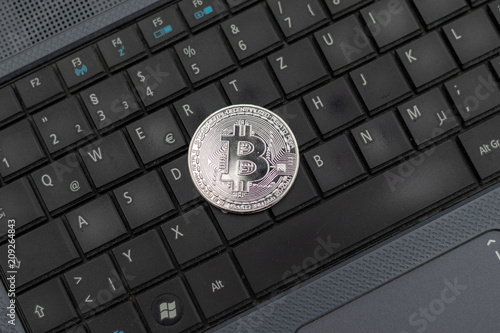 Silver bitcoin coin lying on the keyboard of a laptop 