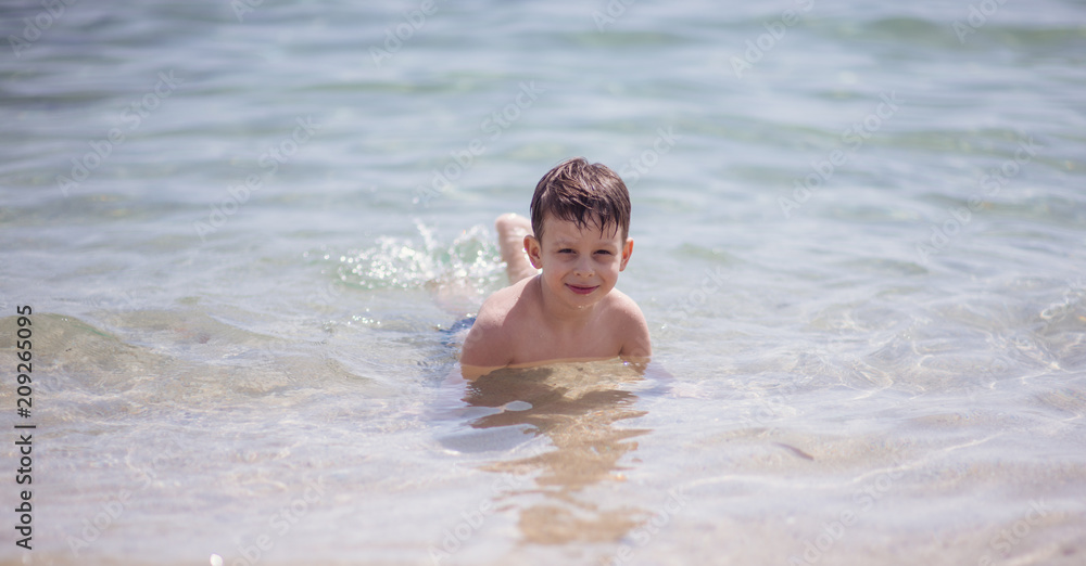 Adorable young kid sitting in the water on the beach