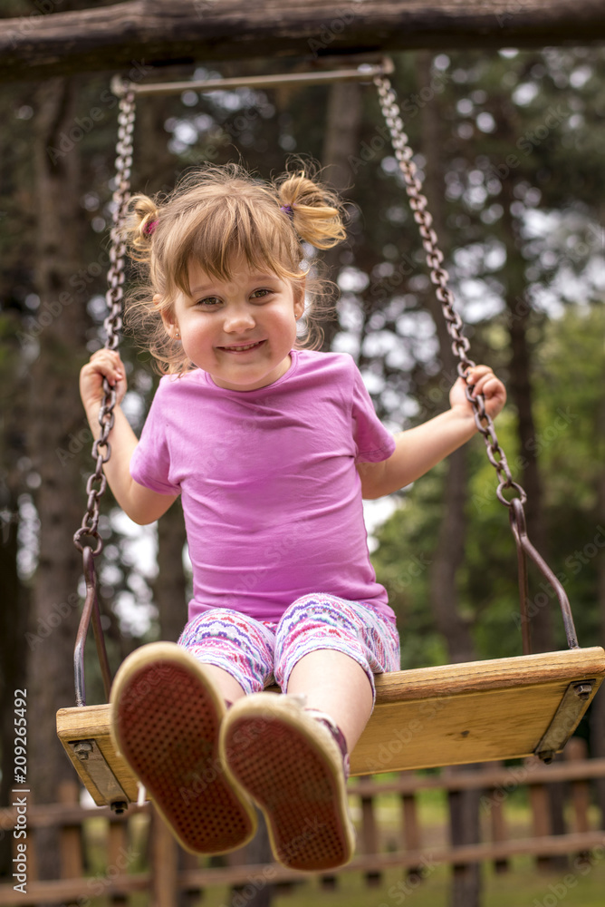 Beautiful child girl smiling and swinging on a swing at the playground Beautiful child girl smiling and swinging on a swing at the playground