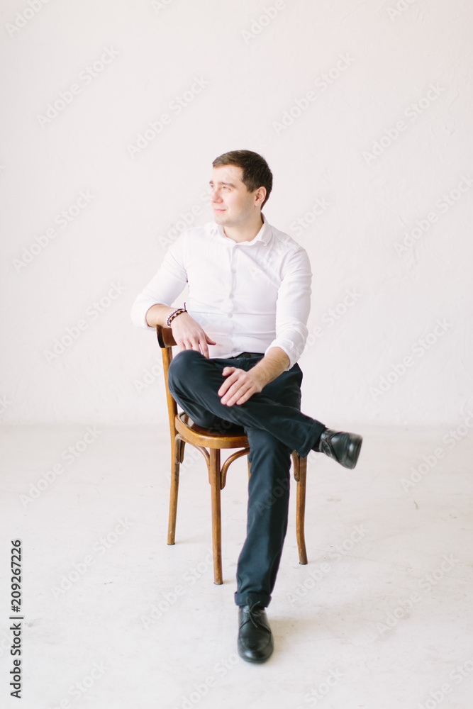 Handsome young groom in Studio with natural light. Wedding photo shoot in European style. Smiling man sitting on the chair.