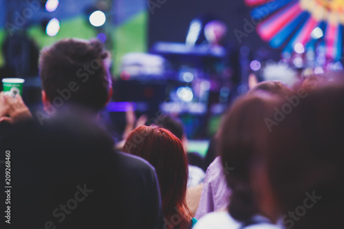 A crowded concert hall with scene stage lights, rock show performance, with people silhouette and hand holding smartphone