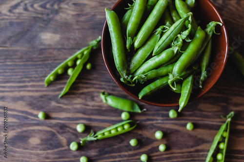 Pods of green peas in a ceramic bowl on a wooden table. Top view.