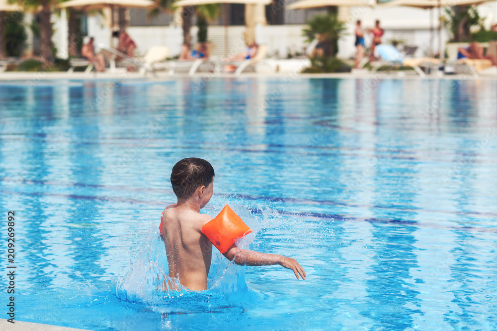 European boy in floating sleeves jumping into swimming pool.