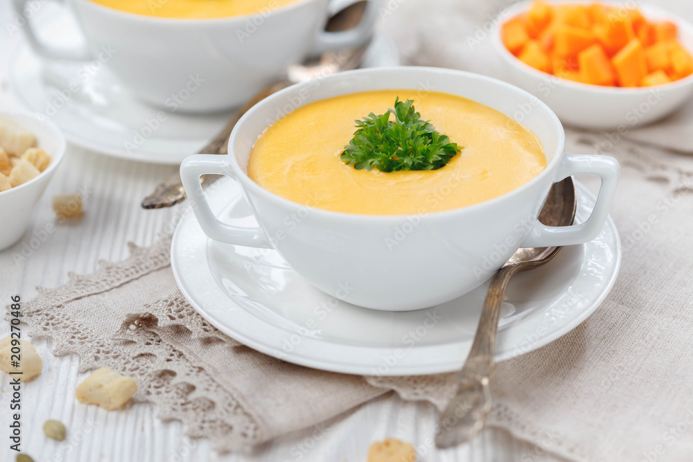 Pumpkin cream soup with croutons, raw fresh pumpkin pieces and herbs on a white rustic wooden background, Autumn concept. Pumpkin cream soup with croutons, raw fresh pumpkin pieces and herbs on a white rustic wooden background, Autumn concept.