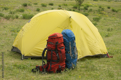Two tourist backpacks near the yellow tent in a mountainous area