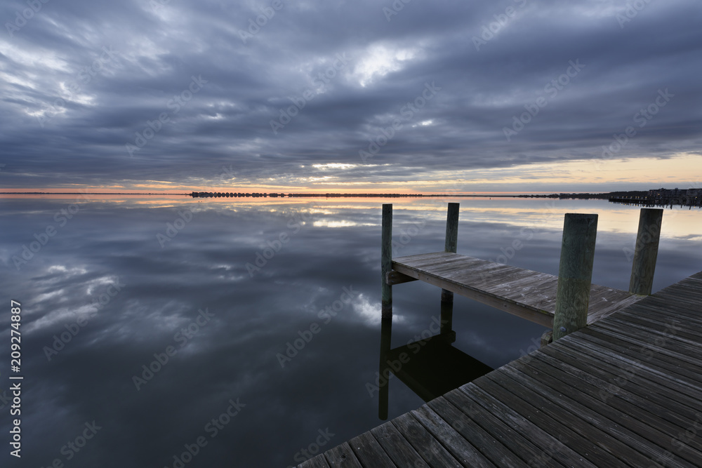 Dock on Ocean Inlet with Dramatic Clouds Reflecting in Water