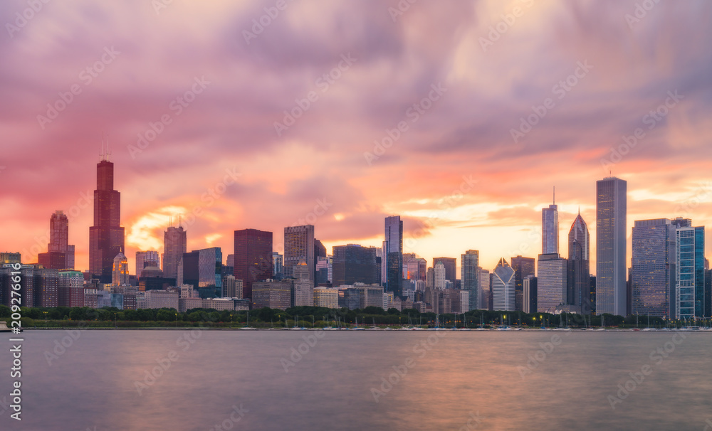  Chicago skyline at sunset with cloudy sky and reflection in water.
