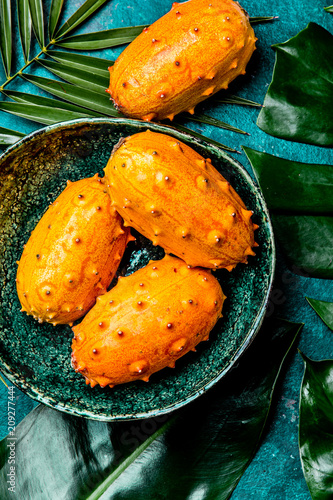 Tropical fruin KIWANO passion fruit in green bowl on turquoise background with tropical palm tree leaves. Top view. Tropical concept photo