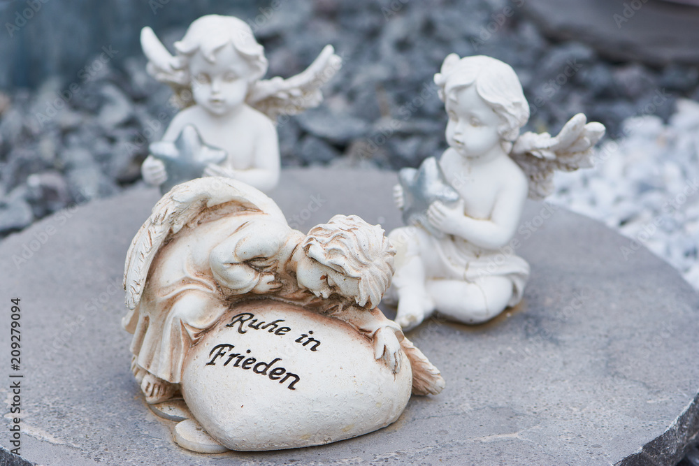 Engel mit einem Herz mit dem deutschen Text "Ruhe in Frieden" und zwei