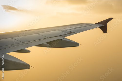 Wing of an airplane flying above the clouds. people looks at the orange sky from the window of the plane when sunset