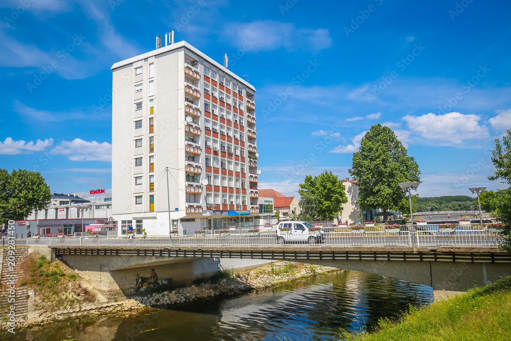 View of a car driving on the bridge across river Vuka with a residential building in Vukovar, Croatia.