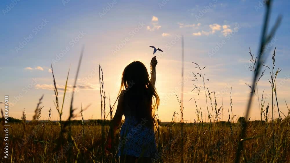 Happy little girl playing with a paper airplane outdoors during sunset ...