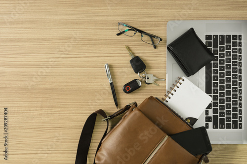 Men's leather bag with personal items and laptop on wood desk.