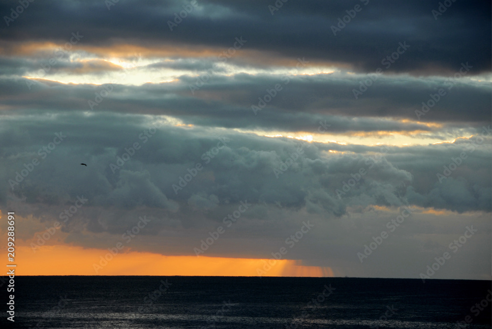 sun setting behind dark clouds over orange sky above dark sea
