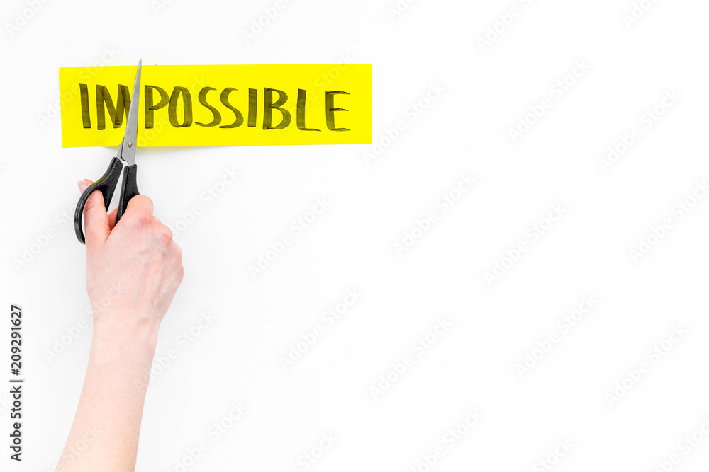 All is possible concept. Hands cutting the part im of written word impossible by sciccors. White background top view copy space All is possible concept. Hands cutting the part im of written word impossible by sciccors. White background top view copy space