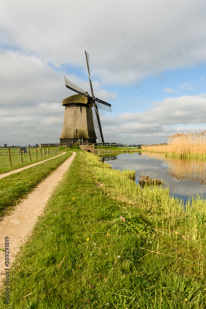 Windmill stands next to a canal in the countryside with a path leading to it in West Friesland, Netherlands