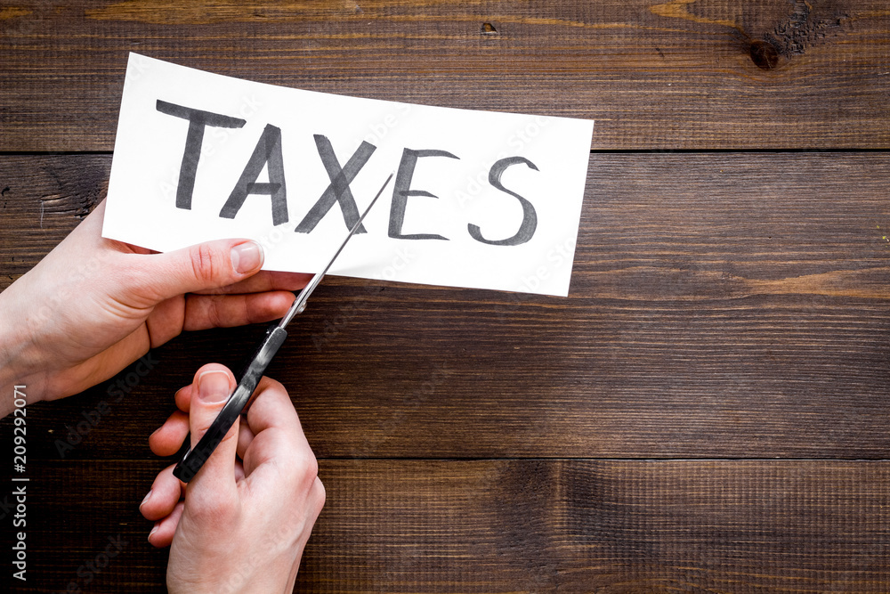 Tax reduce concept. Hands with sciccors cut paper with word Taxes on dark wooden background top view copy space Tax reduce concept. Hands with sciccors cut paper with word Taxes on dark wooden background top view copy space