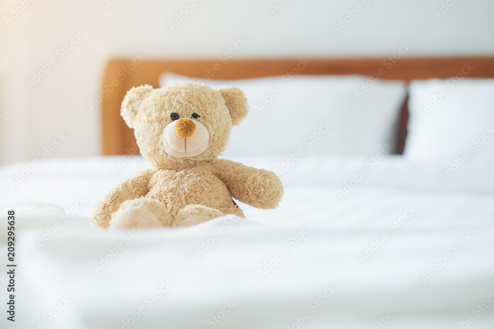 Cute little teddy bear sitting alone on white bed in morning.