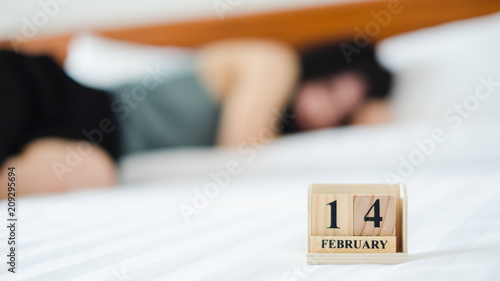 Alone woman sleeping on white bed with 14 February wooden calendar in Valentine day. Broken heart and sad concept.