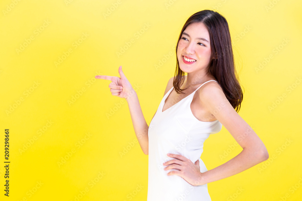 Asian cute woman pointing hands to empty copy space and posing arms akimbo isolated on yellow background Asian cute woman pointing hands to empty copy space and posing arms akimbo isolated on yellow background