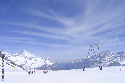 ski resort in the Swiss Alps; a group of people on a gentle ski slope; mountain peaks in the distance