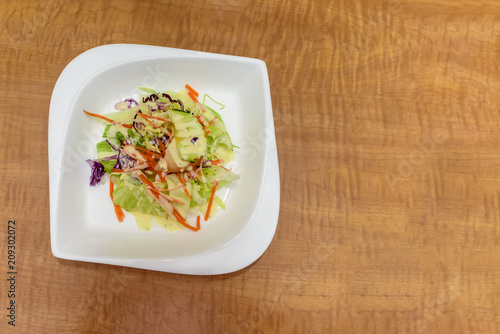 salad of fresh vegetables on a white porcelain plate on a brown wooden table